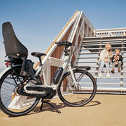 Urban Iki achterzitje Ta-ke MIK HD voor fiets, bevestigd op de achterdrager, met veiligheidsriem en comfortabele zitting.