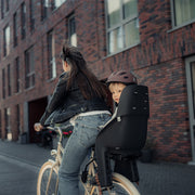 Urban Iki achterzitje U-me MIK HD voor fiets, bevestigd op het achterdrijf, met comfortabele zitting en veiligheidsriemen.